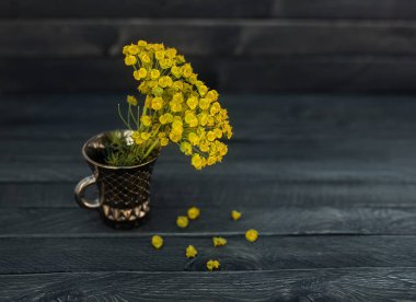 Sarı çiçekler yaldızlı bir fincanda duruyor ahşap bir arka planda.