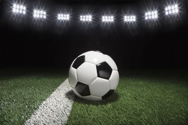 Традиционный футбольный мяч на травяном поле под огнями ночью — стоковое фото