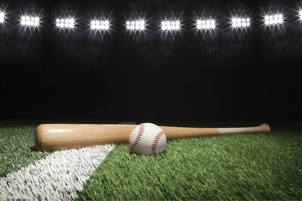 Бейсбол и летучая мышь ночью под огнями стадиона на траве — стоковое фото