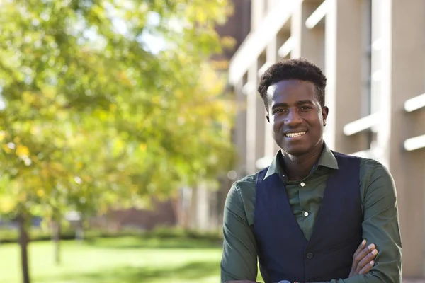 Knappe jonge zwarte student man glimlacht permanent op colege campu Stockfoto