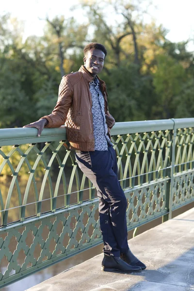 Bonito jovem negro se inclina no corrimão de uma ponte — Fotografia de Stock