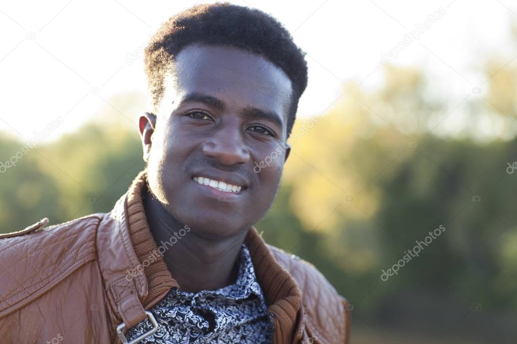 Handsome young black man smiling with defocused trees in the bac
