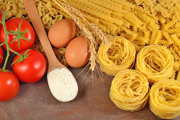 Pastas italianas sin cocer, rama de tomates maduros, harina y huevos — Foto de Stock