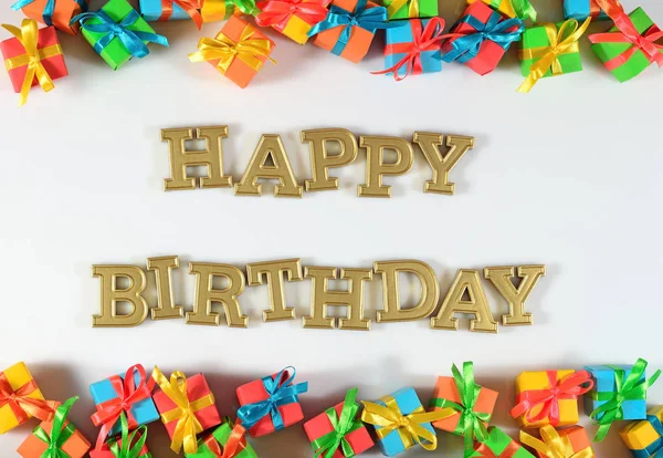 Feliz aniversário texto dourado e presentes coloridos em um branco — Fotografia de Stock