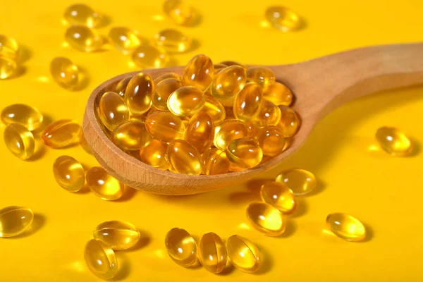 Omega-3 kapsul minyak lemak ikan dalam sendok kayu pada kuning — Stok Foto