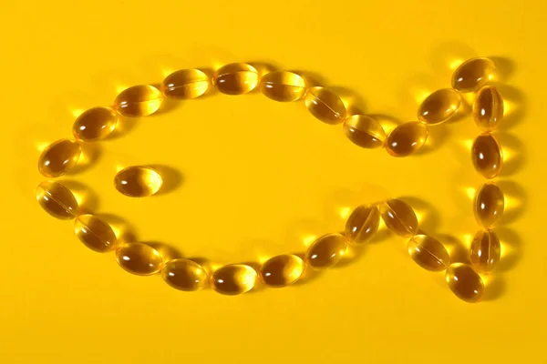 Omega-3 fish fat oil capsules shaped in fish on a yellow