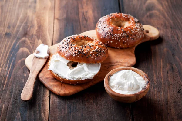 Bagels de grão inteiro com queijo creme na tábua de madeira — Fotografia de Stock