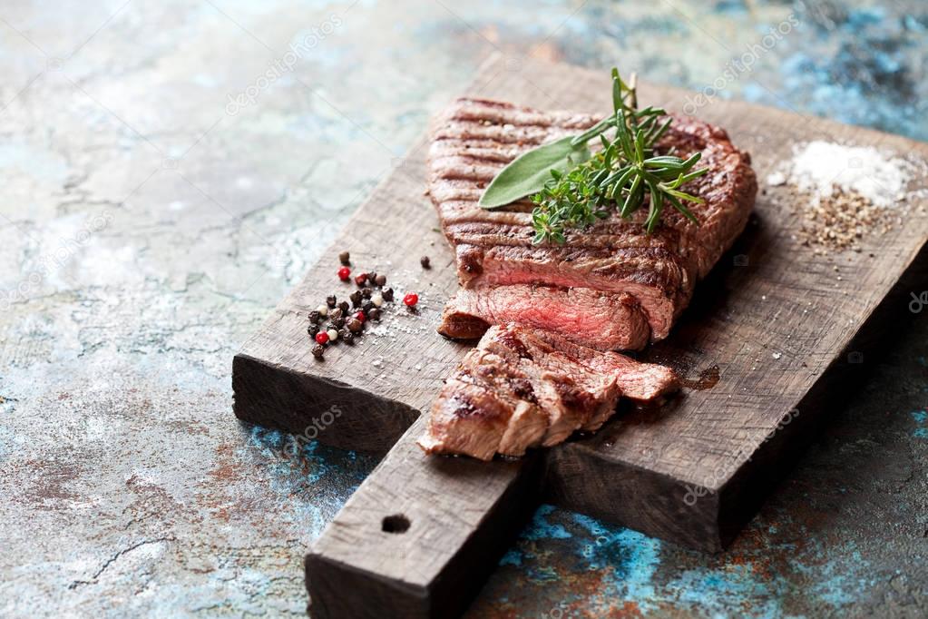 Sliced medium rare grilled beef steak on wooden cutting board
