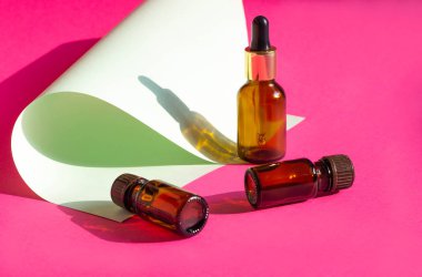 Açık pembe arka planda koyu gölgeli cam kozmetik şişeler. Güzellik blogcusu, prosedür salonu konsepti. Minimalizm. Pembe arka planda kozmetik düşürücü.