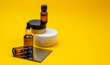 Serumlu kozmetik ürünler seti, parlak sarı bir arka planda ayna ile yüz kremi. Güzellik blogcusu, prosedür salonu konsepti. Minimalizm