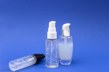 Serum, jöle ve mavi arka planda yüz kremi olan kozmetik şişeleri. Deri kozmetiği, minimalizm. Salon prosedürleri kavramı
