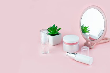 Serum, jöle, pembe arka planda yüz kremi, çiçek ve ayna olan kozmetik şişeler. Deri kozmetiği, minimalizm