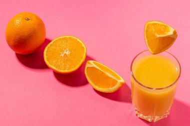 Bir bardak portakal suyu ve dilimlenmiş portakal, parlak pembe arka planda, sert gölgelerle. Taze sıkılmış portakal suyu. Minimalizm