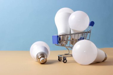 Mavi arka planda bir alışveriş arabasında LED ampuller. Enerji Saklama Ampulleri Alınıyor.