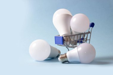 Mavi arka planda bir alışveriş arabasında LED ampuller. Enerji Saklama Ampulleri Alınıyor.