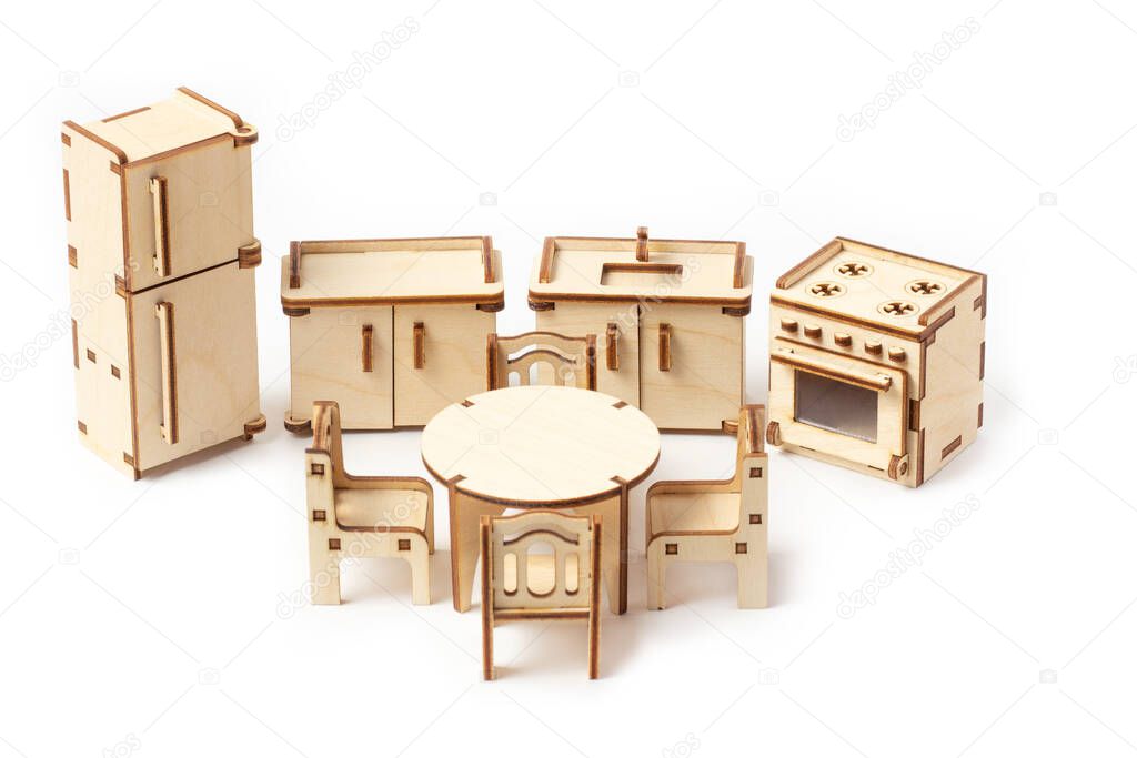 Toy miniature wooden kitchen furniture stands on a white background. Refrigerator, gas stove, sink and dining table with chairs. Furniture for dolls and dollhouse.