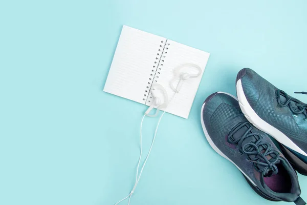 Sports flat layout. Fitness accessories sneakers, headphones and an open notebook for recording on a blue background. Sports Planning.