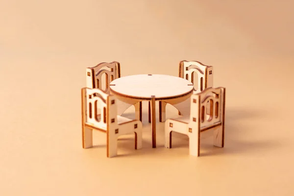 Um conjunto de móveis de madeira em miniatura de brinquedo fica em um fundo bege. Mesa de jantar e quatro cadeiras. Mobiliário para bonecas e casas de bonecas — Fotografia de Stock