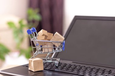 Alışveriş sepeti ve kutular dizüstü bilgisayar klavyesinde. Evden çıkmadan internetten alışveriş yapmak..