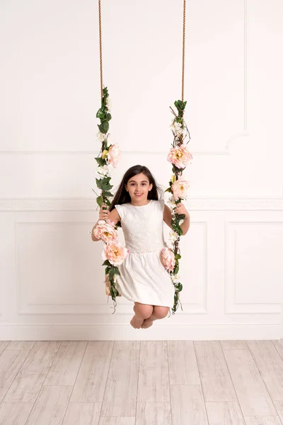 Cheerful girl playing on swing in bright room — Stock Photo, Image