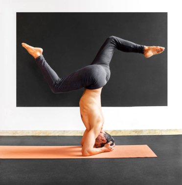 Adam sirsasana varyasyon yoga amfisi yapıyor.