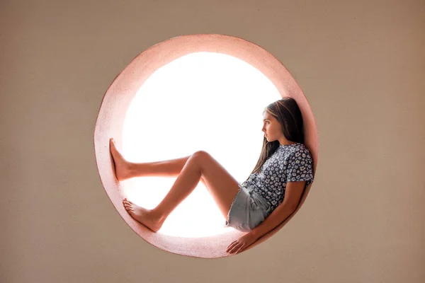 Young barefoot girl curled inside a round opening — ストック写真