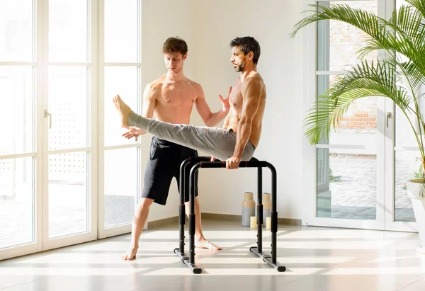 Dwóch Atletycznych Mężczyzn Ćwiczących Gimnastykę Jednym Pomagającym Drugiemu Ćwiczącym Sit — Zdjęcie stockowe