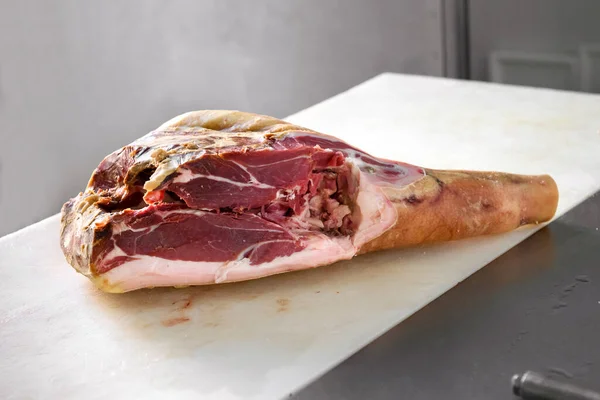 Piece of Prosciutto uncooked ham meat in a butcher shop, viewed in close-up on white cutting table