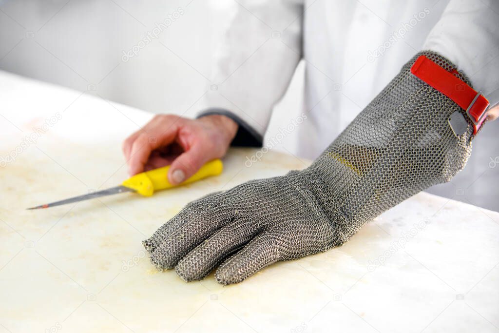 Close up on a chain mail butchers protective glove with metal mesh to prevent cuts from knives on the hand of a male butcher resting on a cutting board