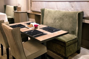 Yeşil pelüş koltuklu şık bir restoran masası ve yemek için hazır gümüş çatal bıçaklı siyah dekor yeri ayarları.