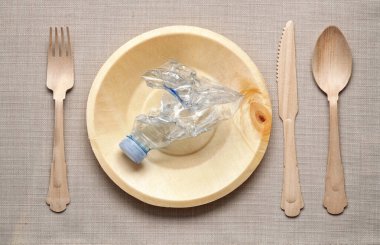 Eş bıçak, çatal ve kaşıkla çevrelenmiş, buruşuk bir plastik şişeyle, masa düzeniyle plastik konsept yemek.