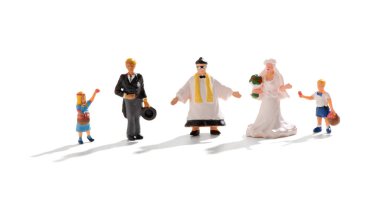 Papazla gelin ve damat arasında duran minyatür insanlardan oluşan bir düğün grubu ve genç bir çiçekçi kız ve beyaz üzerine sayfa görevlisi.