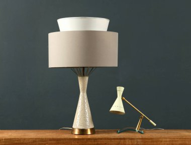 Ahşap bir dolapta iki klasik lamba, biri açısal tabanlı ve gölgeli bir silindir ve koyu gri bir duvara karşı küçük bir fener.