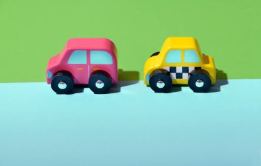 Pembe ve sarı renkli iki parlak ahşap oyuncak araba iki farklı renk yeşil ve mavi arkaplan ve altında kopya alanı var.
