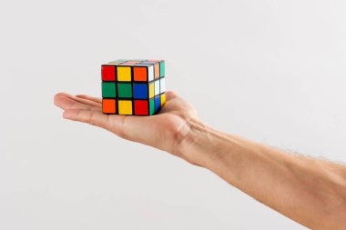 Avucunun içinde çözülmemiş bir Rubiks küp yapbozu tutan adam arka planda beyaz bir duvara uzandı.