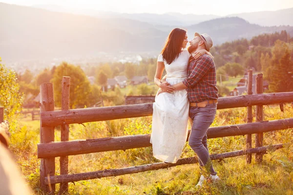 Casal amoroso nas montanhas perto de uma cerca de madeira . — Fotografia de Stock