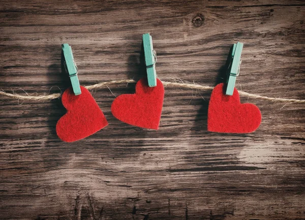 Drei rote Herzen hängen an einer Schnur auf einem hölzernen Hintergrund — Stockfoto