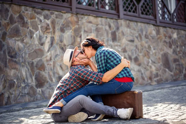 Šťastný pár v lásce sedí na silnici s kufrem — Stock fotografie