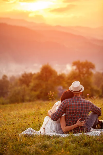 Felice coppia amorevole seduta su plaid in campo. sfondo montagne . — Foto Stock