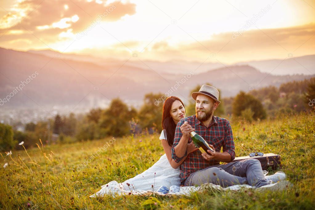 happy loving couple sitting on plaid in field. background mountains.