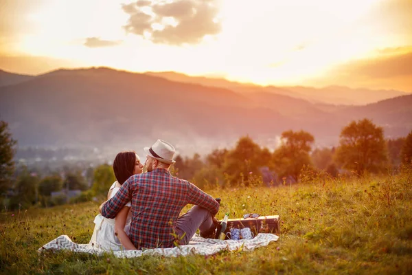 Glückliches Liebespaar, das auf Plaid im Feld sitzt. Hintergrund Berge. — Stockfoto