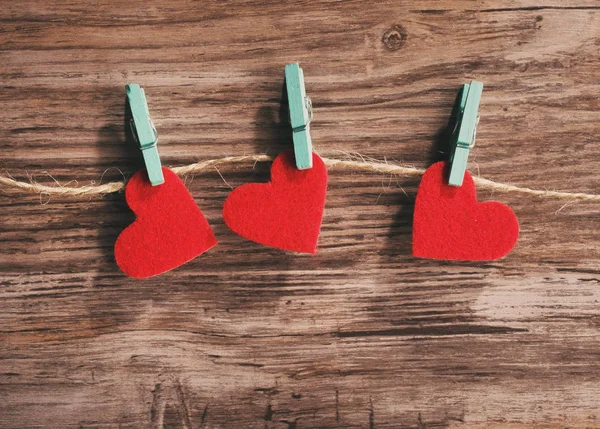Tre røde hjerter hængende på en snor på en træbaggrund - Stock-foto