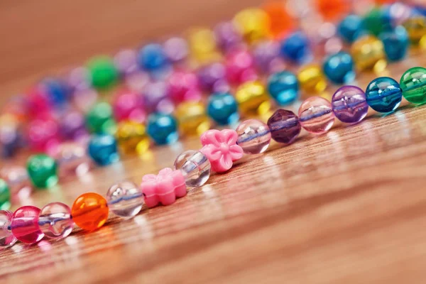 Tejido a partir de un collar de perlas de colores en una mesa de madera . —  Fotos de Stock