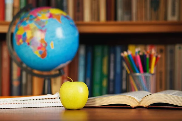 Globe, organisateur, une pomme et un livre ouvert sur la table sur la bibliothèque de fond — Photo