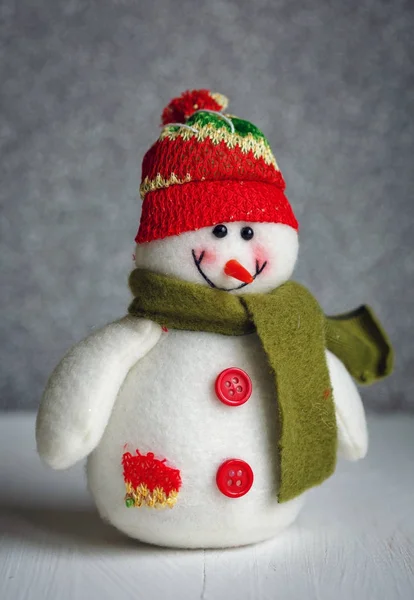 Sorridente pupazzo di neve giocattolo vestito in sciarpa e cappuccio su sfondo bokeh astratto . — Foto Stock