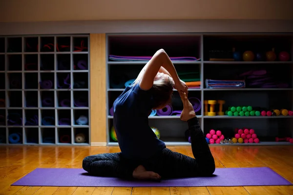 Mooie jonge vrouw trainen in de sportschool interieur, doen yoga oefening op blauw mat, — Stockfoto