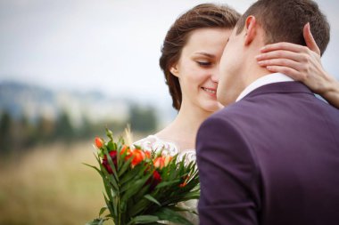 Güzel çift yeni evliler dağlarda. Bir buket ile şık bir gelin damat öper. Güzel ve estetik fotoğraf aşk gösterir.