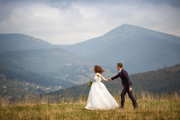 Концепция любви, приключений и природы. Любящая пара, гуляющая по газону на фоне величественных гор . — стоковое фото