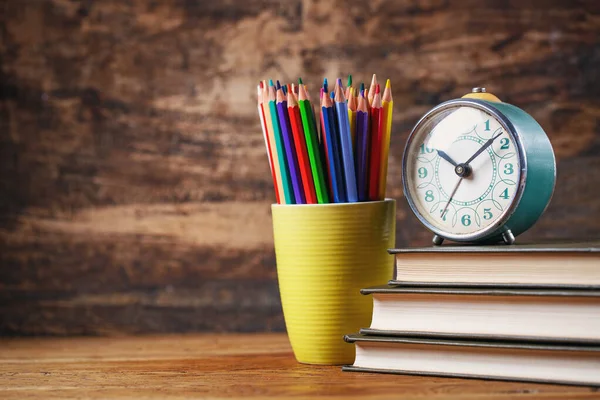 Un viejo reloj en libros de texto cerca con lápices de colores en una taza — Foto de Stock