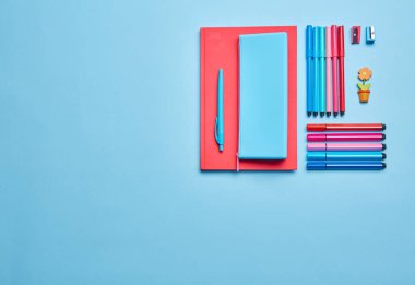 Mavi bir arkaplanda, defterler, kalemler, kalemler, lastikler ve ataçlar. Pembe-mavi gözlüklü. Üst manzara, düz uzanma